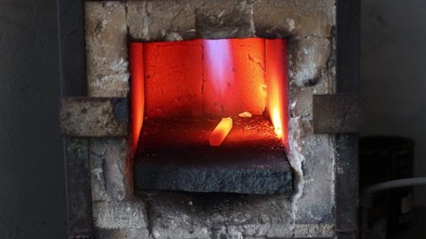 Blacksmith forge oven with hot flame. Smith heating iron piece of steel in fire of red hot forge.