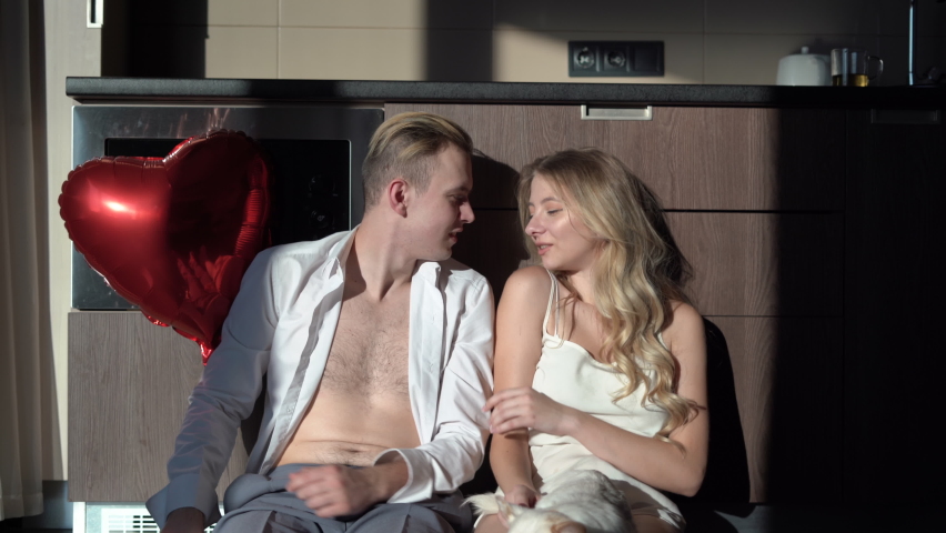 man and woman are sitting in the kitchen in the morning holding a heart-shaped balloon in their hands. The guy gives the girl a gift. concept for celebrating valentine