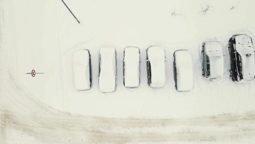 Cars in a parking lot covered with white snow after a blizzard. Aerial view of a city street and standing vehicles as snowdrifts. Sudden precipitation, sharp climate change. UHD 4K.