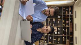 Vertical view multi racial colleagues sit at desk discuss information in document, do paperwork, managing planning expenditures. Couple consider loan, insurance papers, read received notice from bank - Powered by Shutterstock - Get 15% off with code: PIKWIZARD15