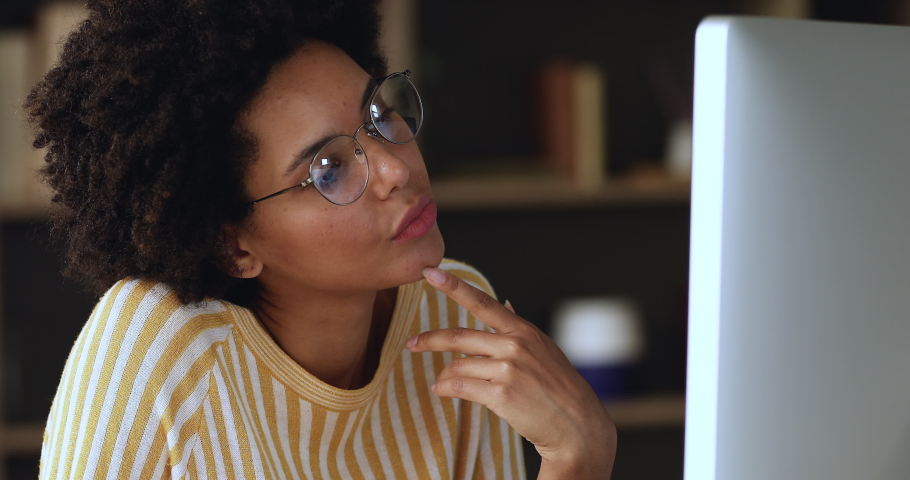 Close up attractive young African woman in glasses sit at desk looks at pc screen, working on computer looks pensive and thoughtful, thinking over solution, search business ideas, do telework concept Royalty-Free Stock Footage #1085842343