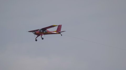 Red small sport plane flying in the sky pulls on a rope the glider plane.