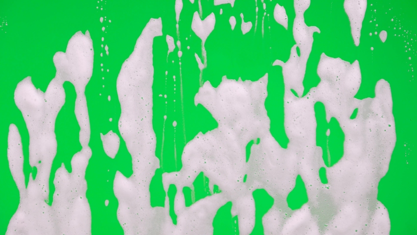White soap suds flowing down window glass on green screen chroma key background. Cleaning windows with cleaning disinfectant. Hygiene, disinfection, housework, household, cleanup, washing. Close up. Royalty-Free Stock Footage #1085846054