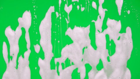 White soap suds flowing down window glass on green screen chroma key background. Cleaning windows with cleaning disinfectant. Hygiene, disinfection, housework, household, cleanup, washing. Close up.