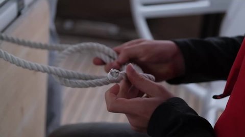 Woman ties complicated knot of rope working on yacht
