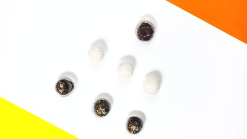 4k Round chocolate candies on a white background with yellow and orange accents. Sweet dessert concept. Stop motion animation. Copy space. Flat lay.
