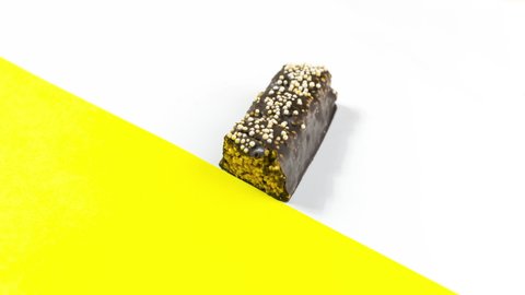 4k On white background with a yellow accent, a rectangular chocolate candy close up appears and gradually disappears as it is eaten. Sweet dessert concept. Stop motion animation. Copy space. Flat lay