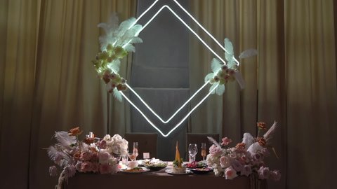 Served table in restaurant for dinner or celebration. Tablecloth, plates, napkins and glasses, chairs. Holiday indoors. Empty with no people and food. Decorated with pink flowers and light wedding.