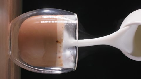 cappuccinos, delicious aromatic coffee drink pours milk foam from a milk jug in a transparent glass, vertical