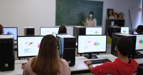 Multiracial young students and teacher wearing safety face masks during coronavirus outbreak inside computer class room at university