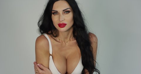 latina woman shows her big beautiful breasts in the studio on a white background of slow motion, red camera. Brunette with red lips