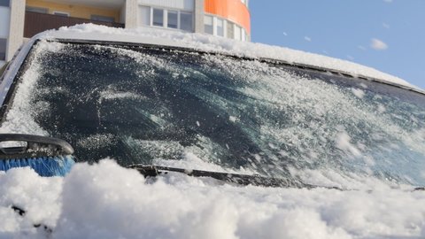 a manual car brush sweeps snow from the hood of a car on a sunny day. Slow motion. Cleaning the car from snow in winter.