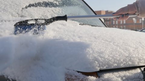 removing snow from a car with a manual brush on a sunny winter day. Close-up, slow motion.