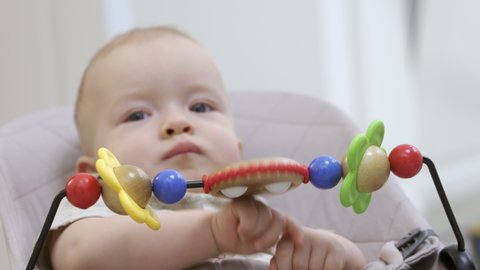 Toddler relaxing in a rocking chair with wooden toys on toy bar, cute baby boy using legs and arm muscles to spring up and down, child face close-up. High quality 4k footage