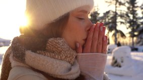 Close-up face of frozen young woman in winter outwear waiting outside in cold windy weather, rubbing hands, blowing on palms to keep warm, suffering from low temperature, on background of sunlights. - Powered by Shutterstock - Get 15% off with code: PIKWIZARD15