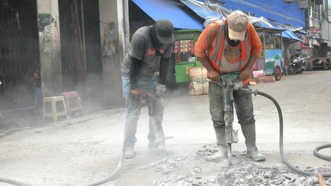 Two men use jack hammer on a street construction project (Jakarta, Indonesia - January 2022).