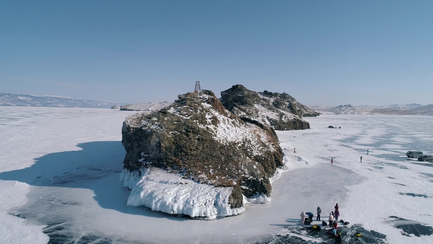 Aerial over the rocky cliff at lake Baikal. Winter landscape of frozen Baikal. Tourist walking around the cliff. Popular tourist spot