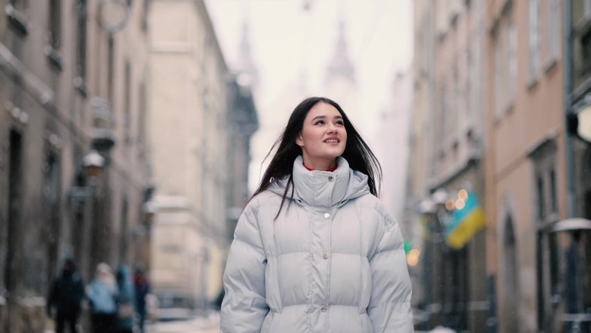 Attractive happy woman walking down the street in snowy city centre. Portrait of beautiful girl in the city street.