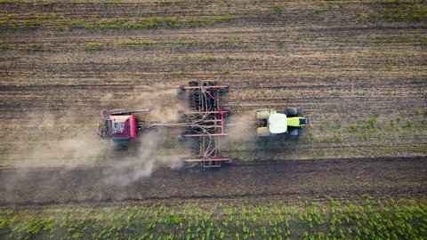 Top down view of tractor sowing seeds with seeder driller in field in late afternoon. Drone shot of agricultural plants and concept of food industry