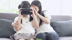 Smiling Asian mother and daughter playing video games with virtual reality headset glasses while sitting on sofa in living room at home. Happy family metaverse VR technology concept. - Powered by Shutterstock - Get 15% off with code: PIKWIZARD15