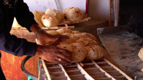 Street bakery, hands of a man putting traditional bread from an oven with traditional Egyptian Bread Aish Baladi