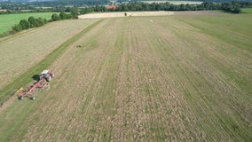 A tractor with a rotary rake rakes hay on agricultural land. Aerial video recording by drone.