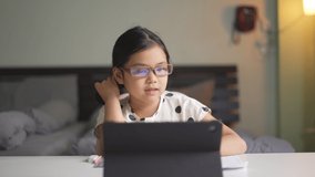 Asian child wearing blue block eyeglasses for fun learning on computer tablet or kid girl student smile to enjoy video call and studying online class or person learn from home school in bedroom