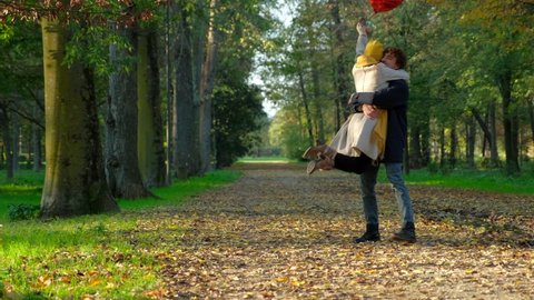 Young couple embracing in park holding red heart-shaped balloon