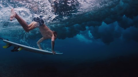 Surfing in Maldives. Teen boy dives with surf board underwater to pass the ocean wave