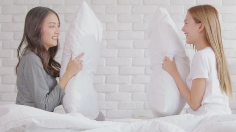 Asian young lesbian LGBTQ couple or friends having fun with play pillows fight together smile and relax at home.Happiness LGBTQ couple woman spending time together at home. LGBTQ Lifestyle Concept