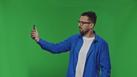 Caucasian young man in glasses having videochat and talking on mobile phoneon isolated background. Video call conversation. Giving thumb up.