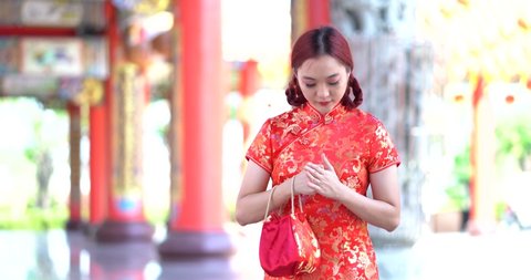 Portrait of young Asian pretty woman in red cheongsam smiling cheerfully to camera and doing Chinese greeting gesture with hands. Beautiful happy girl doing sign of congratulation.