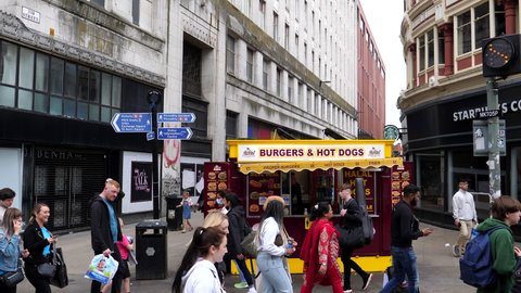 MANCHESTER, ENGLAND, UNITED KINGDOM - CIRCA SEPTEMBER, 2021: People walking past burger and hot dog kiosk on Market and Tib Street junction in the city centre center.