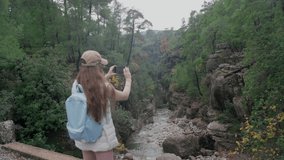 A woman takes pictures on her phone of a beautiful mountain stream in a canyon. Mountain landscape in autumn.