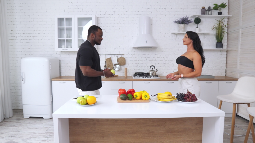 Fitness couple preairing vegeterian dinner. Young strong lifestyle couple in light kitchen.
