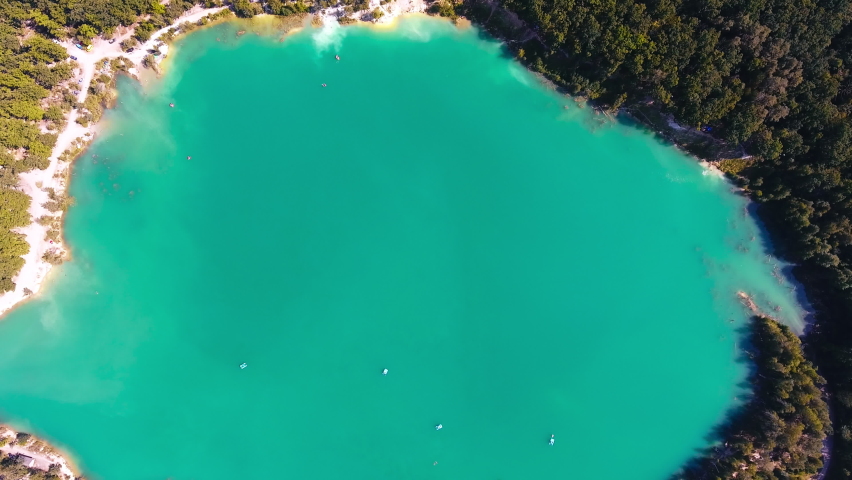 Former kaolin clay mine flooded by water. Few catamarans sailing around the surface. Green thick forests around. Top view.