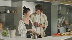 Beautiful and happy couple searching for recipe in internet using cell phone while cooking together on kitchen. Lifestyles with modern gadgets. - Powered by Shutterstock - Get 15% off with code: PIKWIZARD15
