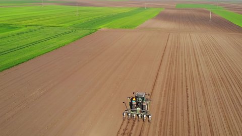 Aerial view of a farmer in tractor seeding and cultivating land, drone shot of sowing agricultural crops at field, around is a fields of green wheat in the spring time
