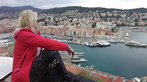 Woman looking Nice French city skyline on Port Lympia. Aerial view of cityscape of NICE with lighthouse from panoramic terrace of Colline du Chateau park in Blue Coast of France.