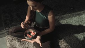 Video of a woman sitting on the floor at home, relaxing and eating a bowl of granola or rolled oats with cranberries. Natural organic nutrition.