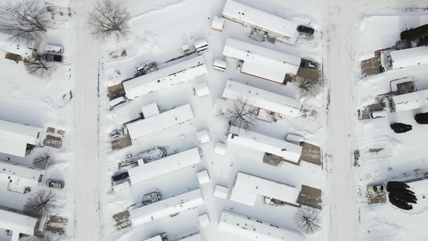 Top down view over snow covered mobile home park on a quiet winter day in Wisconsin. Streets plowed. No people. Vehicles parked by homes. 