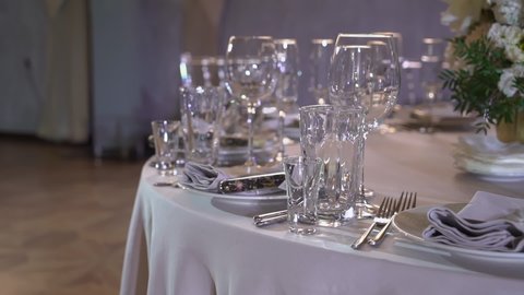 Served table in a restaurant for dinner, lunch or celebration. White tablecloth, plates, napkins and glasses. Holiday indoors. Empty with no people and food. Decorated for wedding.