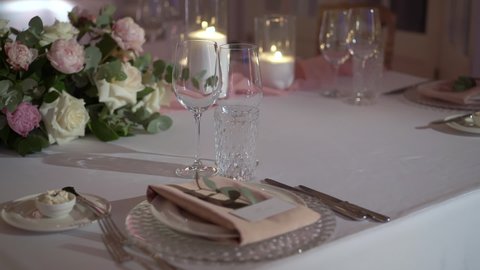 Served table in a restaurant for dinner, lunch or celebration. White tablecloth, plates, napkins and glasses, chairs. Holiday indoors. Empty with no people and food. Decorated with flowers for wedding