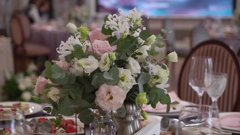 Decorated with pink and white rose flowers for wedding. Served table in a restaurant for dinner, lunch or celebration. White tablecloth, plates, napkins and glasses, chairs. Holiday indoors.