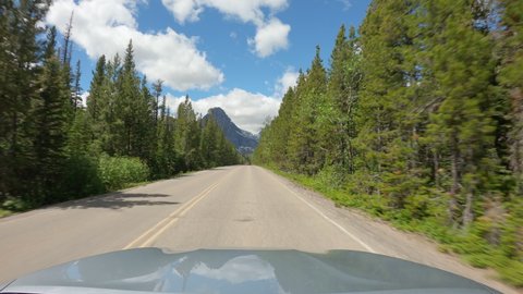 POV Driving a car on asphalt country road with trees in Montana high mountains. Blue sky on sunny day	