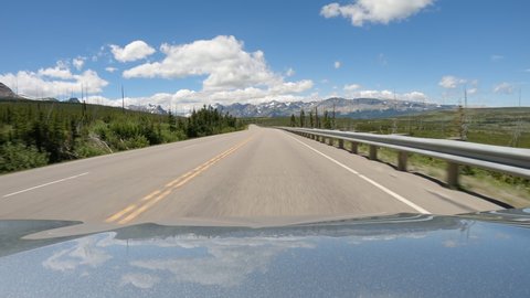 POV Driving a car on asphalt  mountain road towards Glacier Country in Montana. Sunny day with blue sky and white clouds