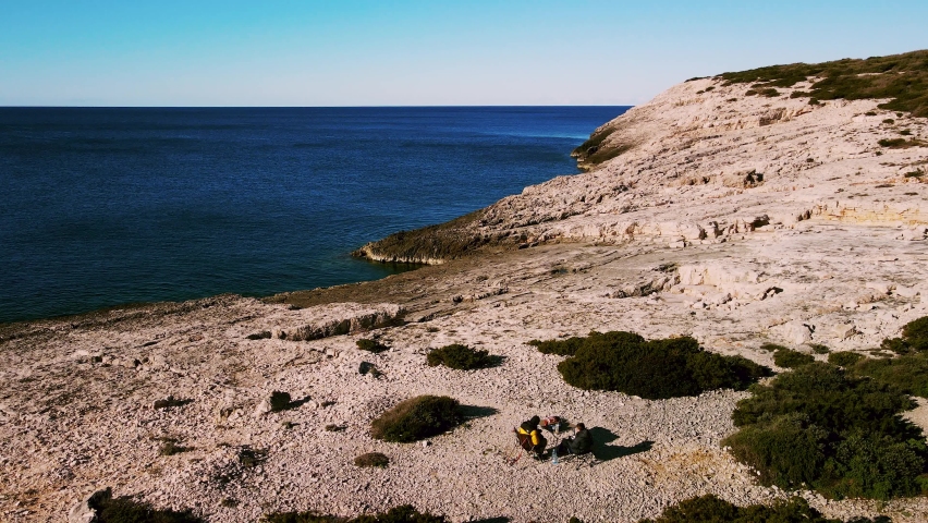 2 Tourists sitting and enjoying the view next on the coastline of fishing town Rukavac, Island Vis, Croatia during the Corona Pandemic. Panoramic view of the rocky landscape with lush green foliage.