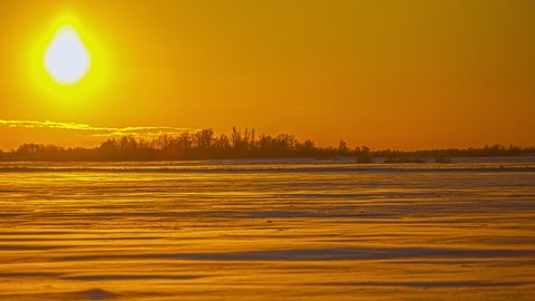 View of bright sunrays reflecting over snow covered meadows in the countryside. Beautiful yellow sunset in timelapse.