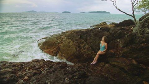 Woman meditates, relaxes on rock crack reef hill in stormy morning cloudy sea. Concept feminine, sexual vaginal health, womanly, freedom, freshness