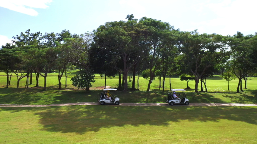 Aerial view group of Asian people businessman and senior CEO sitting on driving golf cart at golf course in sunny day. Healthy male friends golfer golfing together at country club in summer vacation Royalty-Free Stock Footage #1085933021
